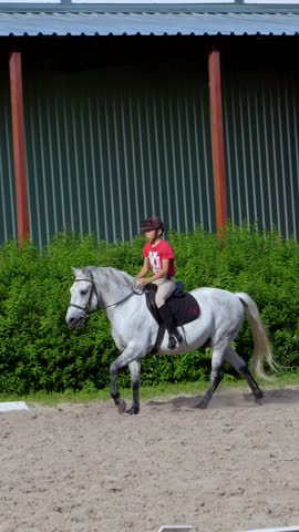 Boy rider, jockey riding on thoroughbred beautiful white stallion, horse, on the training sand field, ground. boy learns to ride a horse in horse riding school. Summer, outdoors