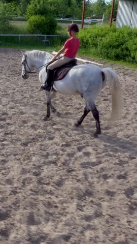 Boy rider, jockey riding on thoroughbred beautiful white stallion, horse, on the training sand field, ground. boy learns to ride a horse in horse riding school. Summer, outdoors