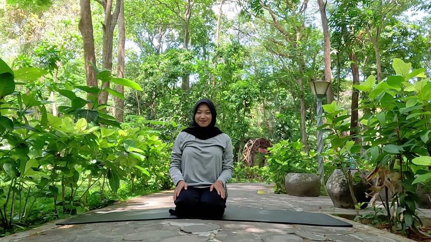 Muslim woman doing yoga in park wearing long sleeve t-shirt and black hijab