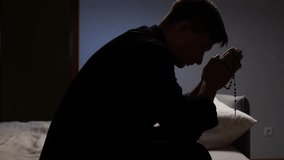 Young priest praying with rosary in dark room - Powered by Shutterstock - Get 15% off with code: PIKWIZARD15