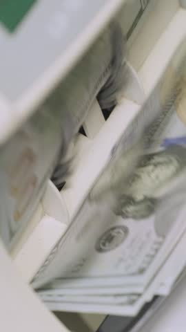 Stacks of US dollars being processed and counted in an automatic money counting machine.