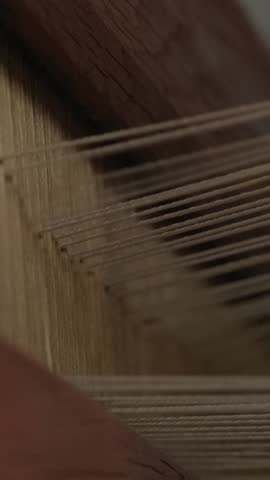 Hands weaving fabric on a traditional wooden loom with threads and natural lighting.