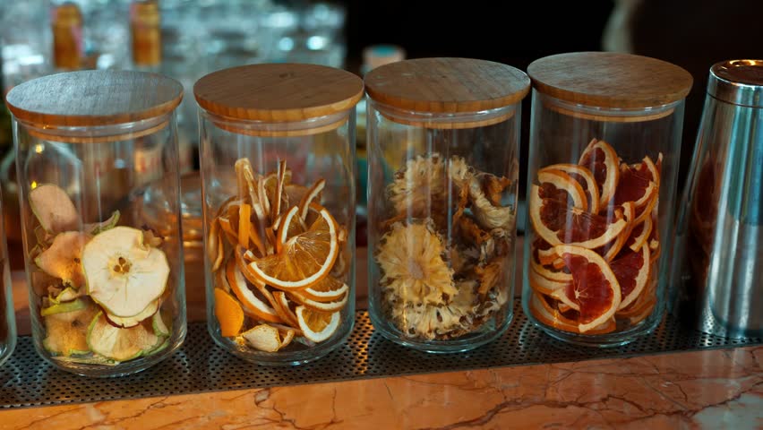 Glass jars filled with dried apple orange pineapple and citrus slices displayed at tropical beach cocktail bar - slow motion parallax