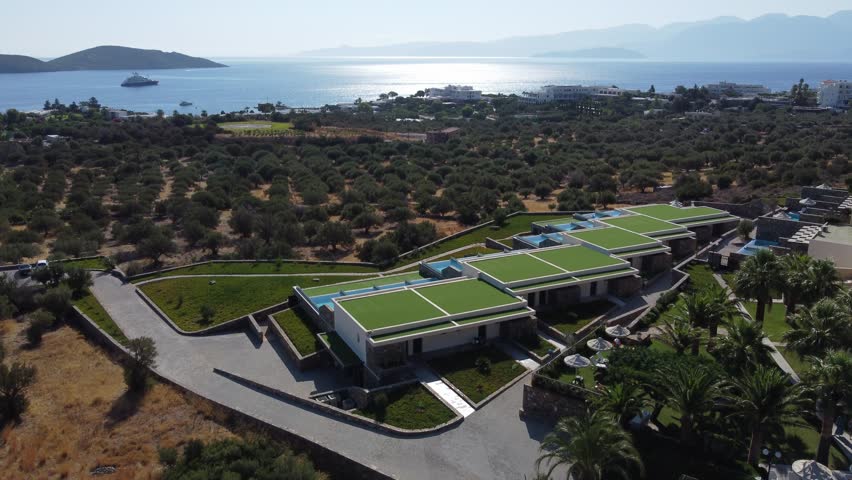 Luxury hotel with outdoor swimming pools facing sea of Crete surrounded by olive groves, Elounda Palm Hotel, Elounda, Establishing drone shot