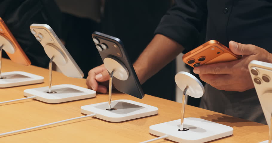 Close-up, shopper comparing smartphones in tech store, holding new phone, deciding to buy. Modern retail gadget purchases, consumer choice, product testing. Man intent shopping decision in shop