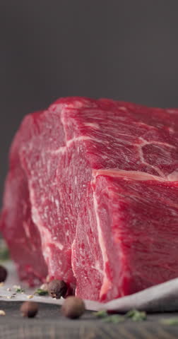 Fresh raw beef meat with pepper and thyme turning on dark wooden cutting board