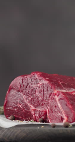 Fresh raw beef meat with pepper and thyme turning on dark wooden cutting board