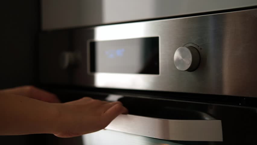 Side view of the woman turning on the electrical oven in the kitchen to baking dessert. Checking readiness of the food