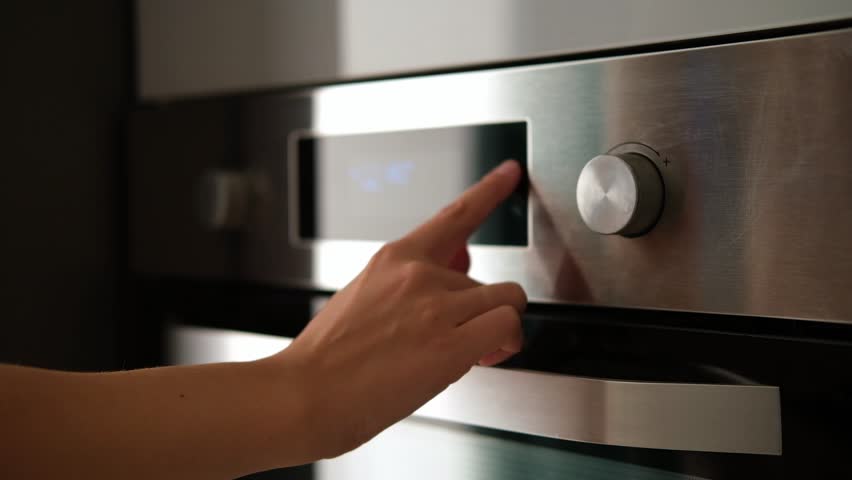 Side view of the woman turning on the electrical oven in the kitchen to baking dessert. Checking readiness of the food