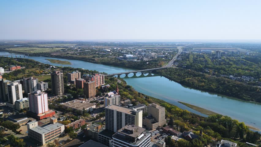 Drone orbit shows Saskatoon bridge, river, downtown skyline, highway stretching