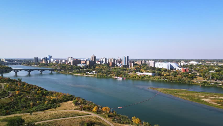 Slow rising aerial reveals Saskatoon downtown, blue sky, fall foliage, bridges
