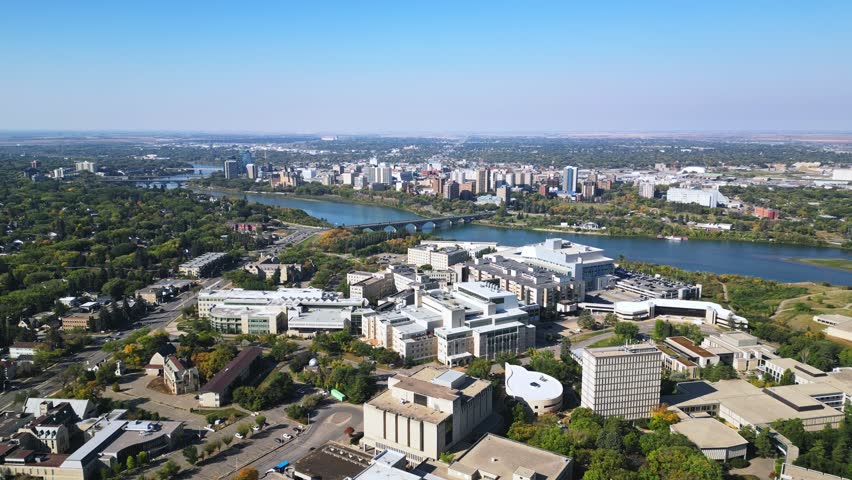 Slow forward aerial over Saskatoon campus in fall, downtown skyline, blue sky