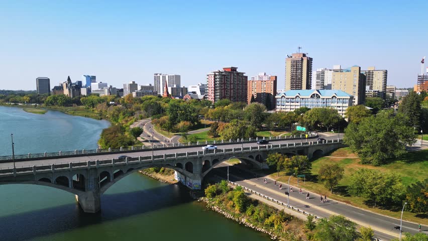 Aerial push-in toward Saskatoon downtown, bridge traffic, riverside jogging path