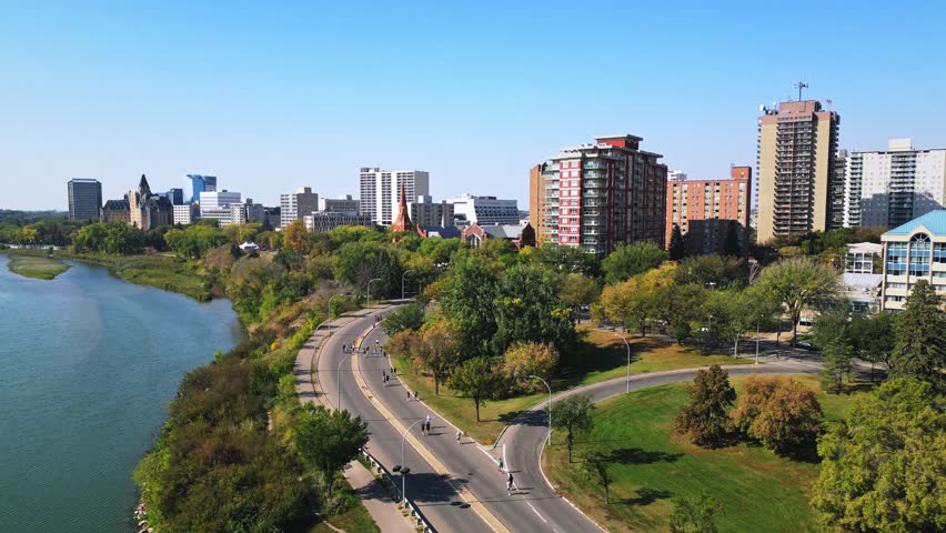 Drone push in shows marathon runners by Saskatoon riverfront under blue sky