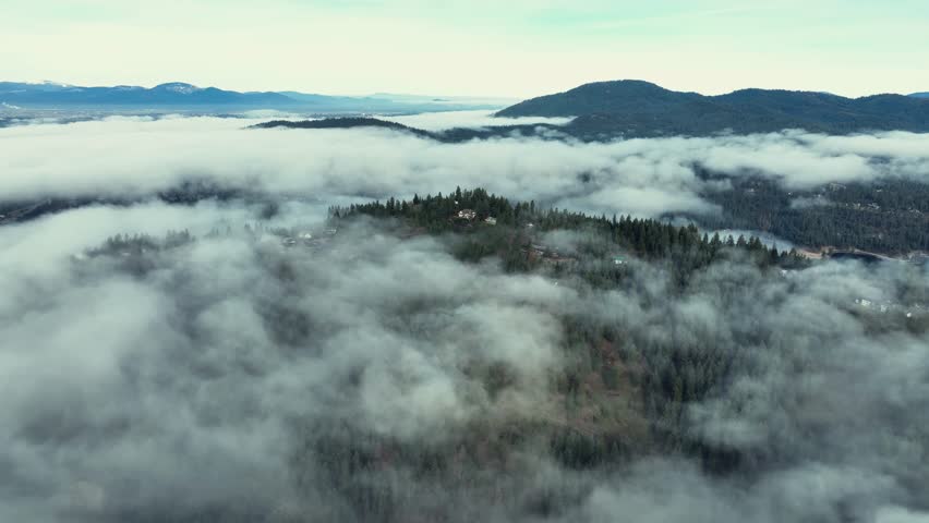 Aerial drone view above the clouds with forest hills, rivers, and houses in Washington State USA