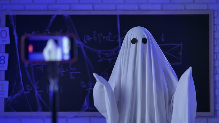 A person dressed in a white sheet like a ghost sits in front of a smartphone and conducts an online lesson