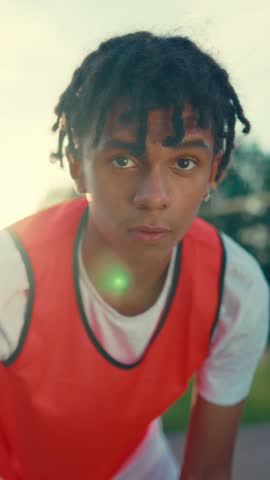 Motivated junior basketball player training alone on street, vertical portrait of black teen boy. Motivated sportsperson looking at camera when practicing with ball, future champion of basketball