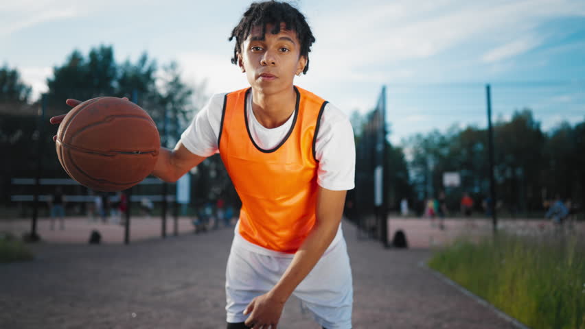 Sportive teen boy playing with ball on streetball court in summer, do sport. Hobby and healthy lifestyle, sport activities for young people, african american teenager looking at camera, champion