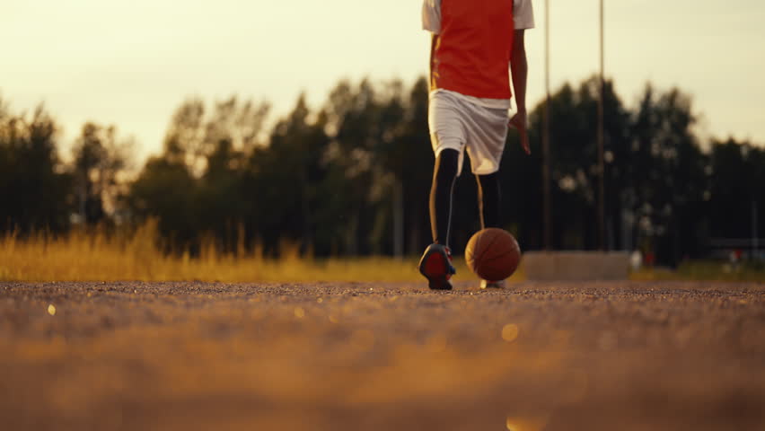 African basketballer walking and bouncing ball in nature, closeup of legs. Footwear for active sport and professional use, energy and power of sport, future champion practicing, move to your dream