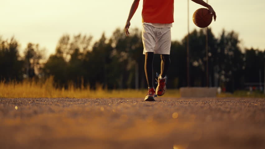 African basketballer walking and bouncing ball in nature, closeup of legs. Footwear for active sport and professional use, energy and power of sport, future champion practicing, move to your dream