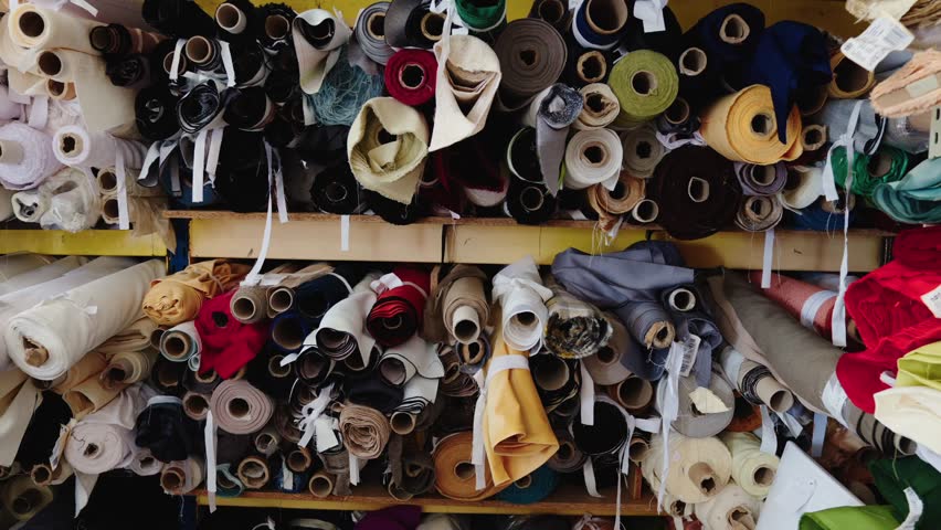 Various colorful fabric rolls neatly stored on shelves in a textile workshop, showcasing materials used in fashion and design production.
