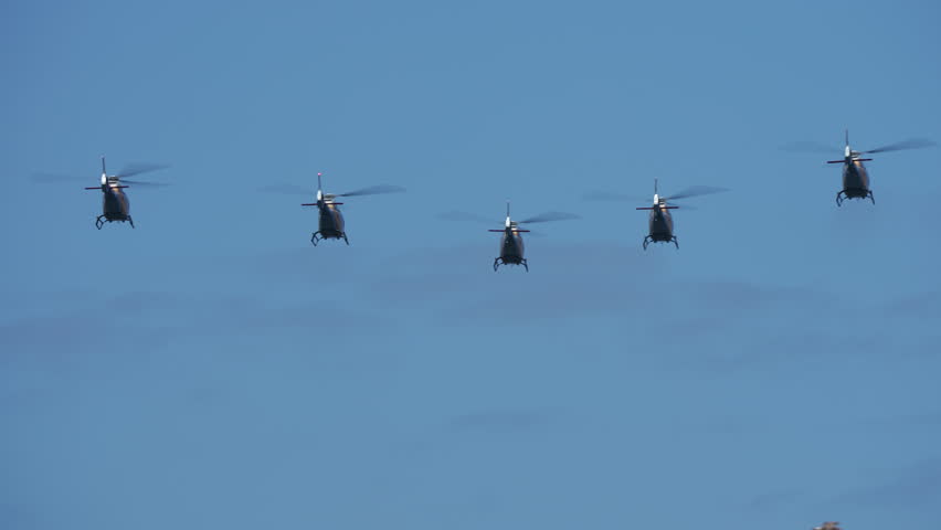 Five military helicopters flying in synchronized formation against blue sky during air show