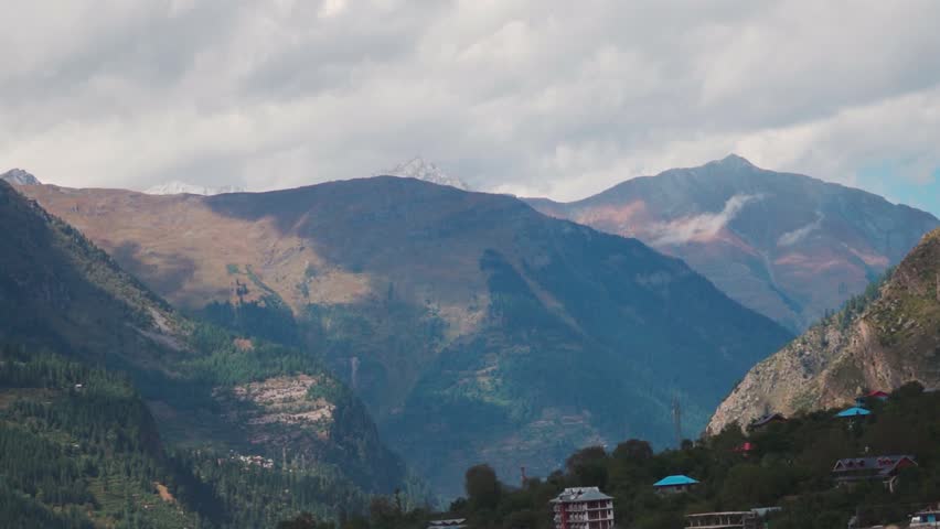 Scenic mountain range with Pine trees on it with clouds above them as seen from Sangla village in Kinnaur district, Himachal Pradesh, India. Scenic view of Himalayas during summer season.