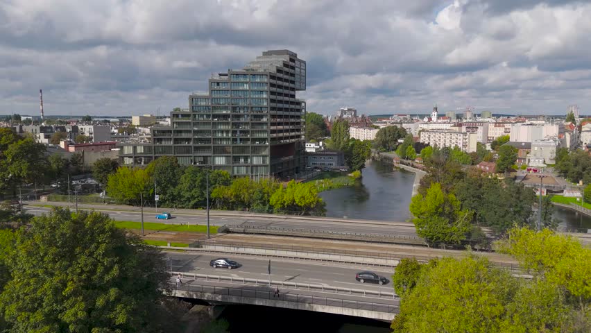 Aerial view of the River Brda flowing through the city with a modern building, surrounded by lush greenery, Bydgoszcz, Kuyavian-Pomeranian Voivodeship, Poland.