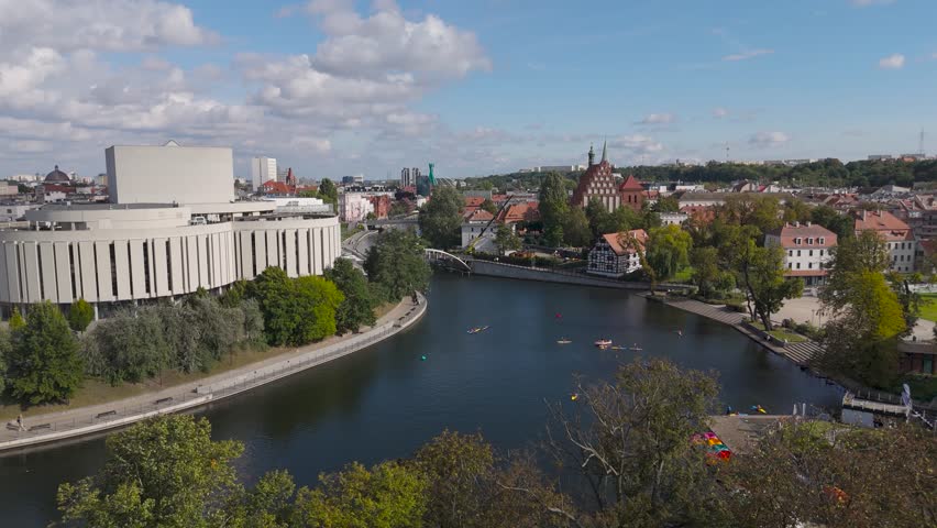 Aerial view of the Opera Nova juxtaposed with the river Brda, where colorful kayaks glide through the dark water, Bydgoszcz, Kuyavian-Pomeranian Voivodeship, Poland.