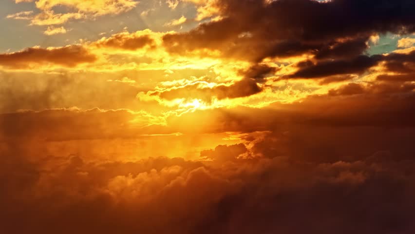 Sunset clouds stretching across golden sky above layered silhouetted hills, aerial heavenly rays pullback