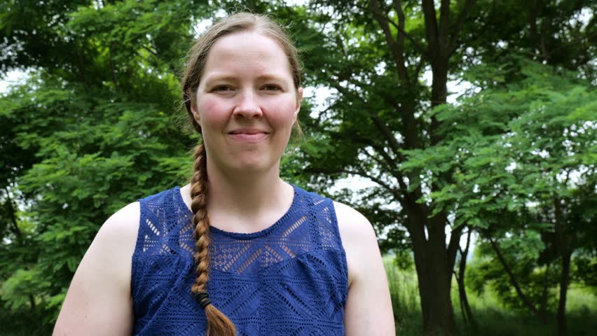 Smiling White Woman Holds Up a Wording Message of Merry Xmas and Points Humorously in front of Trees in the Yard 4K Video Stock Footage