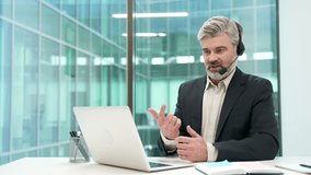 Confident businessman in a headset talking on a video call conference using laptop in office. Manager has a business meeting. Coach has online training, consultation, class, course or webinar remotely - Powered by Shutterstock - Get 15% off with code: PIKWIZARD15