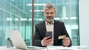 Businessman enters a credit card data on mobile phone sitting at workplace in business office. Entrepreneur in formal suit shopping online, happy about a successful transaction, e-commerce, e-shopping - Powered by Shutterstock - Get 15% off with code: PIKWIZARD15
