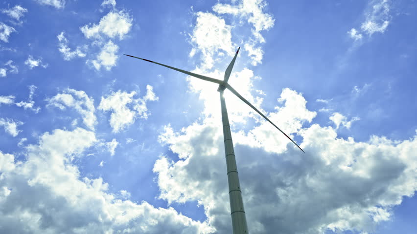 A powerful windmill generates energy against a blue sky. A wind turbine spins against a sky. Energy generation by wind turbines.
