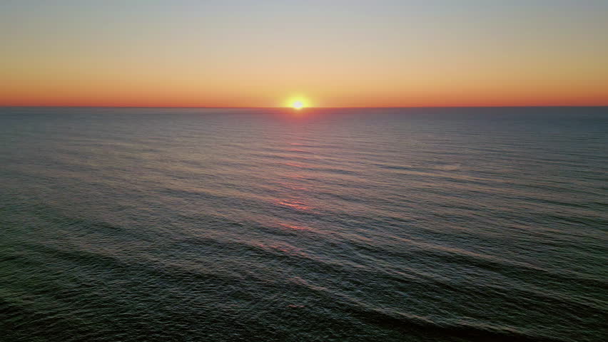 Golden sun setting over marine horizon aerial view. Bright yellow skyline meeting with deep calm ocean surface at summer evening. Panoramic drone shot of idyllic sea sunset. Scenic sunrise landscape.
