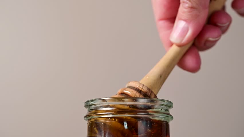 Jar of honey with wooden dipper, sweet liquid, neutral background