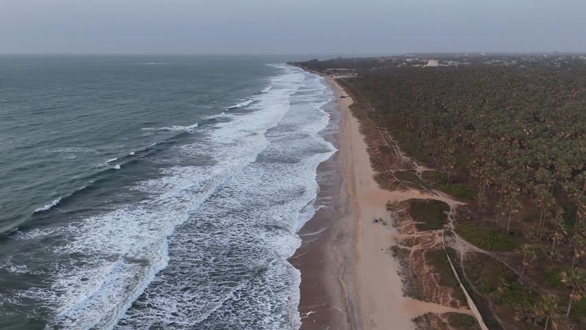 Aerial view of the long beach in Banjul, Gambia, with rolling waves and lush vegetation by the shoreline