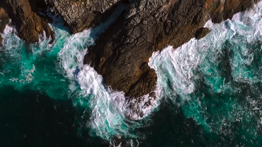 Strong Waves Crashing Against the Rugged Coastline And Cliffs Of Island. - aerial topdown shot