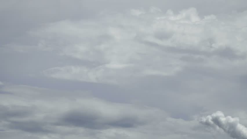 Overcast sky with dense grey and white clouds, featuring a distinct plume of smoke or vapor rising from the bottom right, creating an atmospheric and moody weather scene.