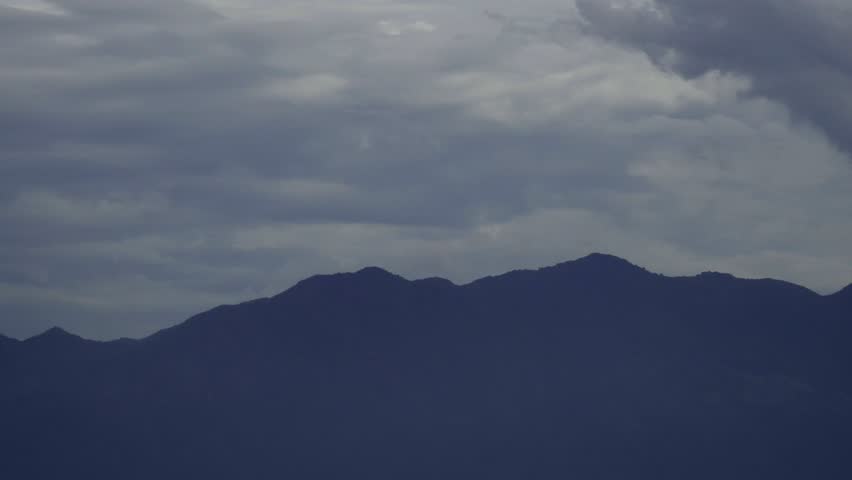 Dark mountain range silhouette under a dramatic cloudy sky at dusk, creating a serene and mysterious natural landscape.
