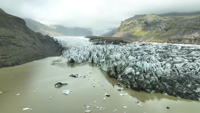 Aerial view of glacier and icebergs on Iceland during cloudy day. Rocky Mountains on Island in Europe. Rising backwards. Global warming in summer.