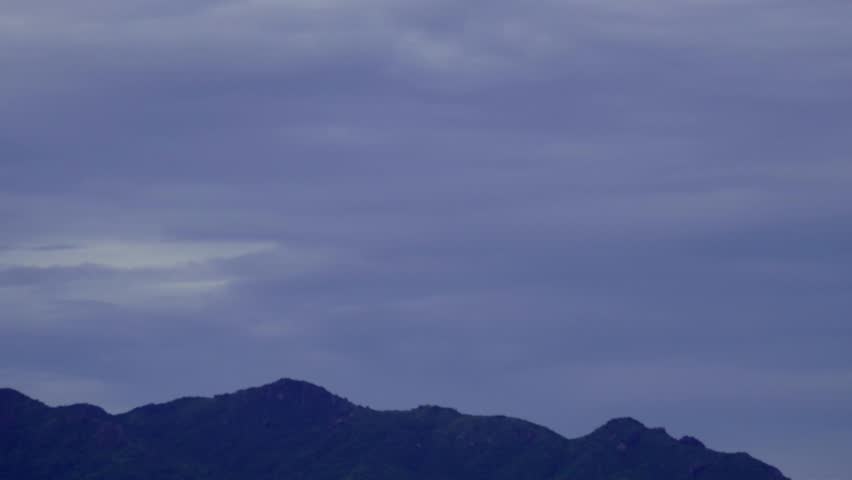 Majestic mountain range silhouetted against a vast, cloudy blue-grey sky, capturing a serene and natural landscape at dusk or dawn.
