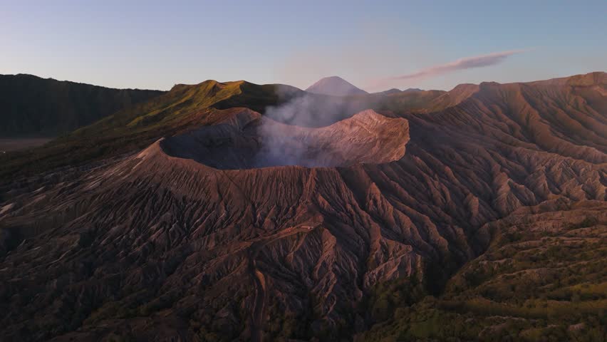 Aerial: Mount Bromo volcano crater with smoke at sunrise in East Java, Indonesia, orbit drone shot