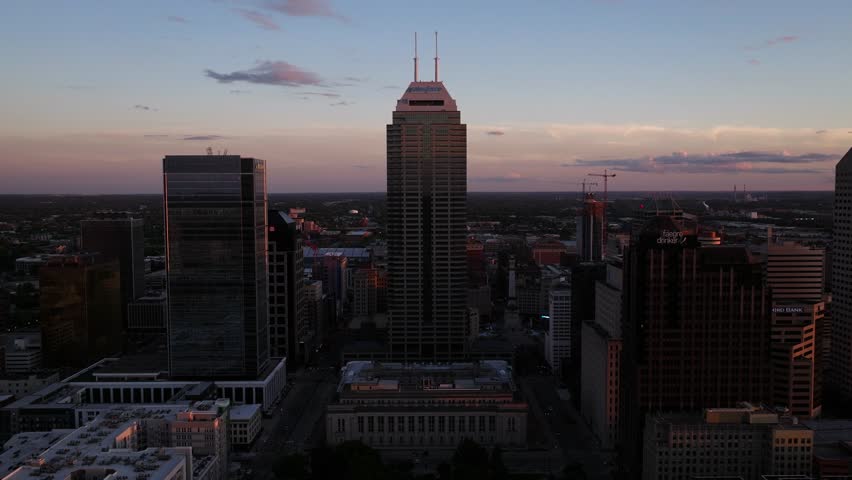 Aerial Pullback Reveals Downtown Indianapolis skyline at sunset on a summer day. City skyscrapers and landmarks in warm evening light.