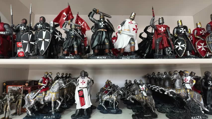 Souvenir figurines of Maltese knights in armor with swords, shields, flags, and horses, displayed on shelves.
