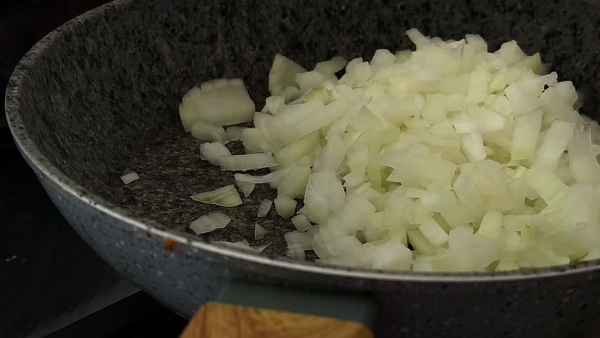 Meal prep process, sauteing chopped onion on a skillet or a frying pan with a wooden spatula. Pouring oil on top. Cooking onions on a gas stovetop. Horizontal, 4K footage