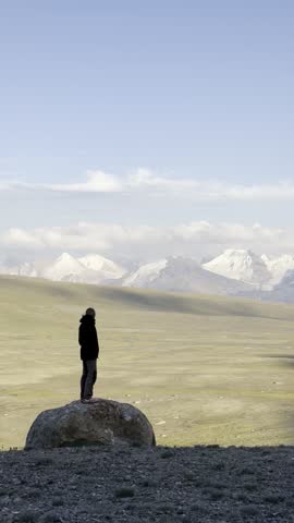 a man stands on a rock and admires the panoramic view of the mountain peaks and the mountain valley