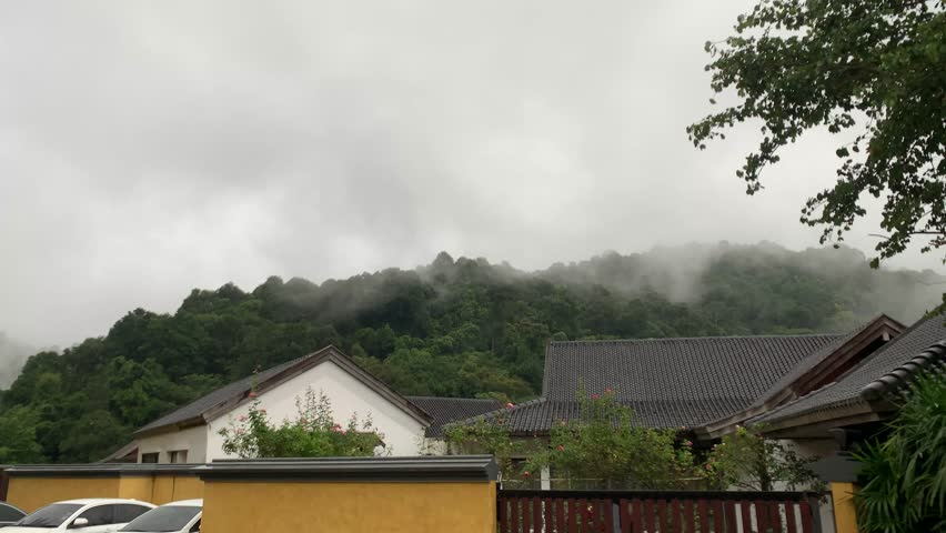 A moody and atmospheric view of a home nestled against a lush, misty mountain range
