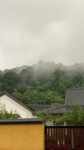 A moody and atmospheric view of a home nestled against a lush, misty mountain range.