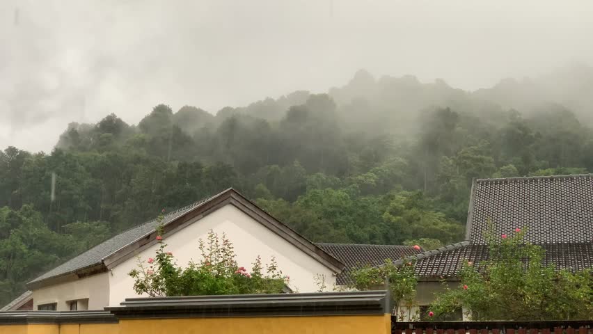 A moody and atmospheric view of a home nestled against a lush, misty mountain range.
